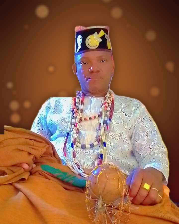 Maître Kpadé en tenue traditionnelle blanche, avec ses colliers de perles et sa calebasse