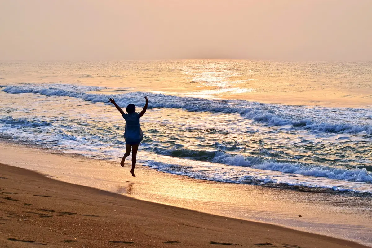 Une personne lève les bras sur la plage de Ouidah au lever du soleil